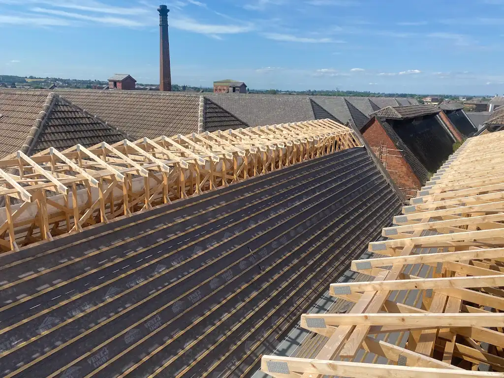 New timber roof trusses beside a tiled roof near a factory chimney