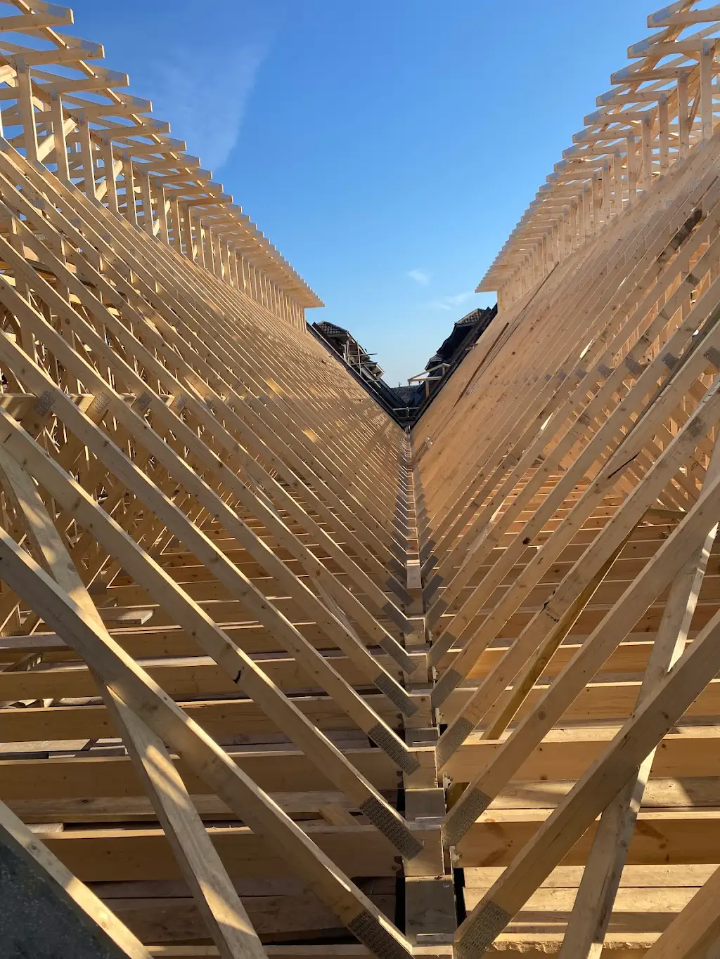 New timber roof trusses between two roof slopes under a blue sky