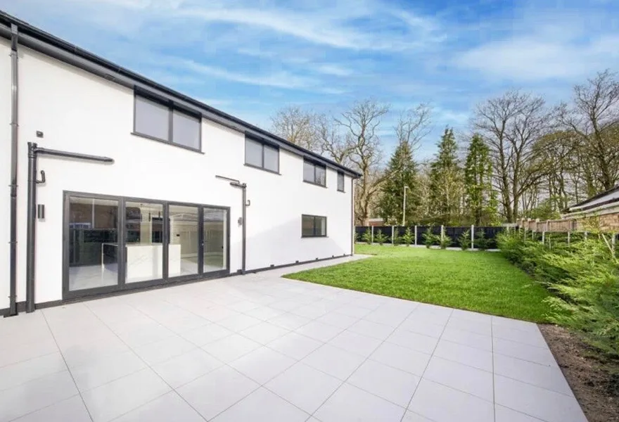 Rear of a white rendered house with sliding doors and a paved patio